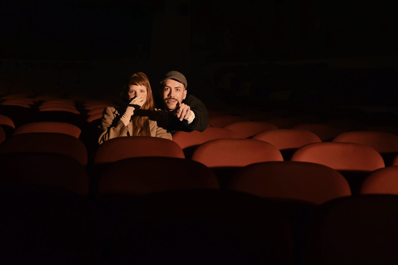 A couple sits in a dimly lit cinema theater, enjoying a movie together.