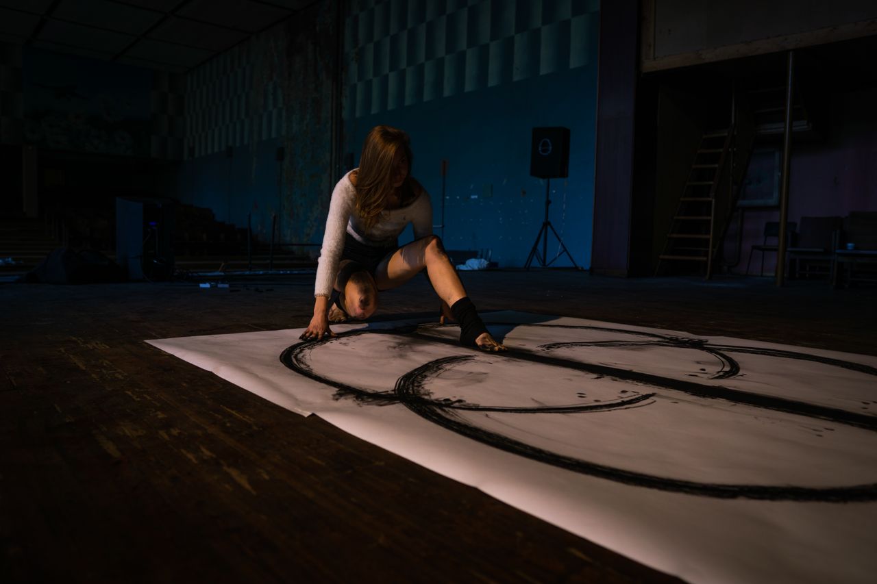 Woman creating artwork with feet in dimly lit art studio, exploring unique artistic expression.